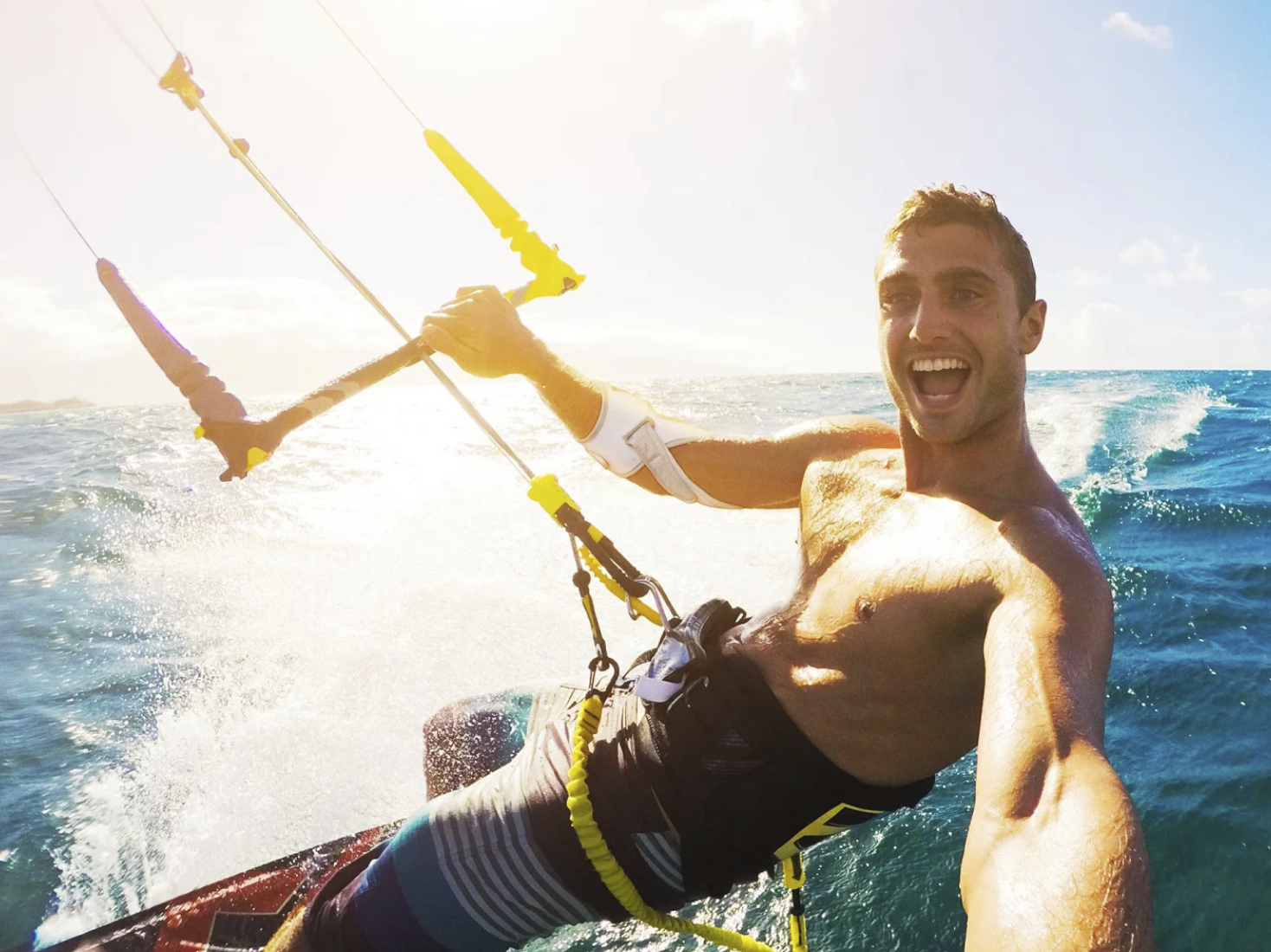 A young, athletic, laughing man wearing the Masalo cuff while kitesurfing in the ocean.